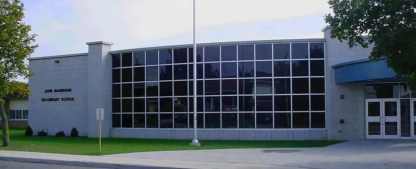 L'edificio moderno a più piani della John McGregor Secondary School sorge su un'area verde con alberi.