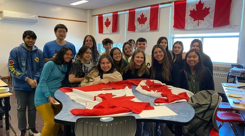 Un gruppo di studenti e studentesse posa insieme in un'aula del campus del St. James Collegiate con bandiere canadesi sullo sfondo.