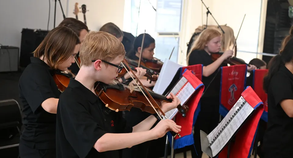 Un gruppo di giovani musicisti della Aspley State High School suona concentrato strumenti ad arco durante un'esibizione.