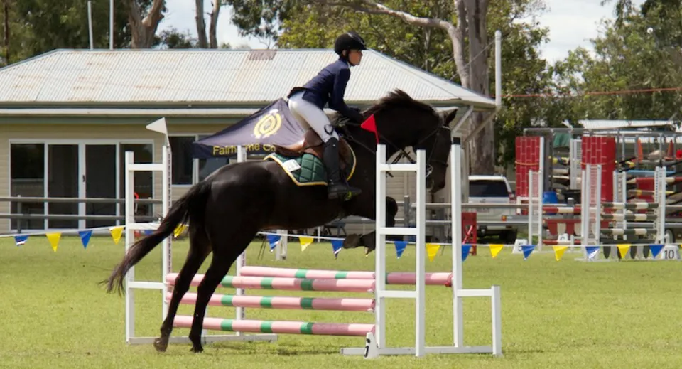 Una studentessa della Mabel Park State High School supera un ostacolo a cavallo su un campo erboso.