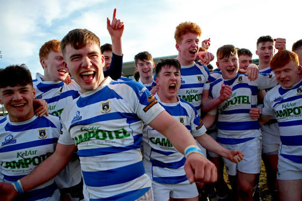 Un gruppo di giovani giocatori di rugby in maglia blu e bianca festeggia sul campo da gioco del Garbally College.
