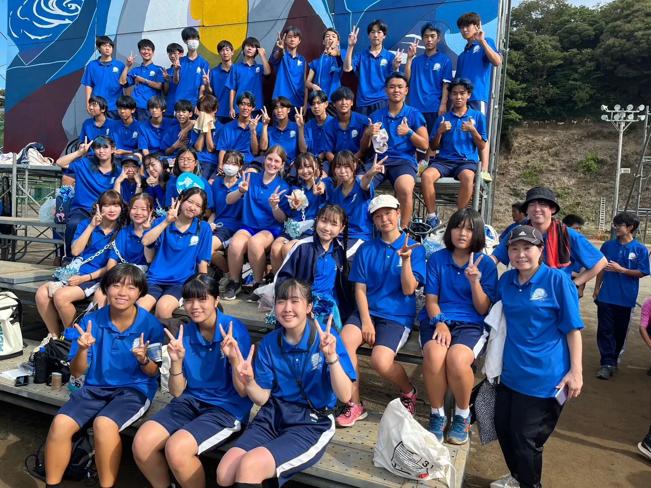 Grande gruppo di studenti giapponesi in tuta sportiva blu posa sorridendo col segno della pace