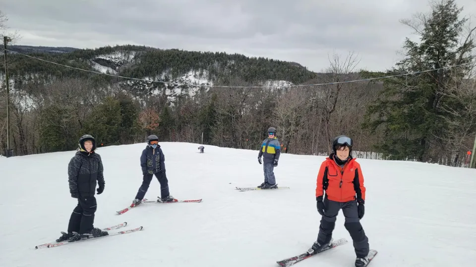 Studenti della École secondaire publique Carrefour Jeunesse mentre sciano su una pista da sci innevata circondata dal bosco.