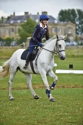 Estudiante con casco montando un caballo blanco en un concurso hípico