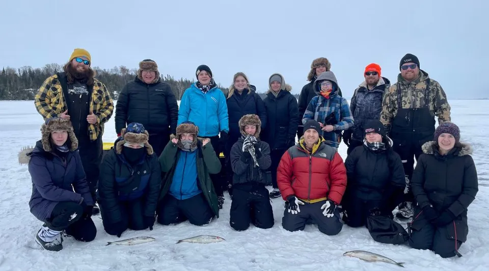 Studenti della Assumption College Catholic High School vestiti con abiti invernali su un campo innevato davanti a un bosco.