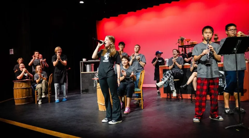Studenti della Holderness School sul palco con strumenti musicali davanti a uno sfondo rosso.