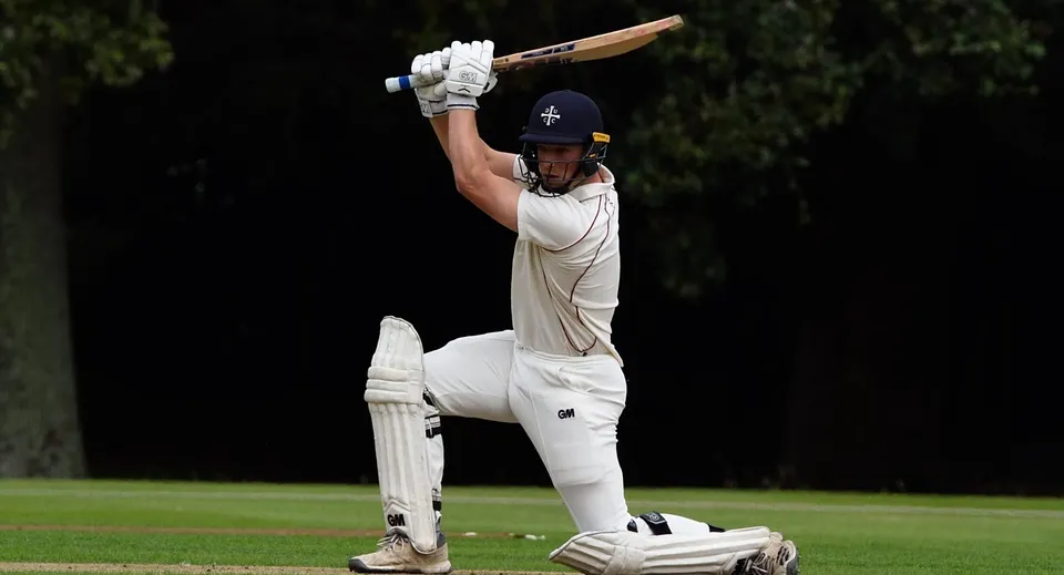 Un giocatore di cricket in divisa bianca sta sul campo da gioco della Bloxham School e si prepara alla battuta.