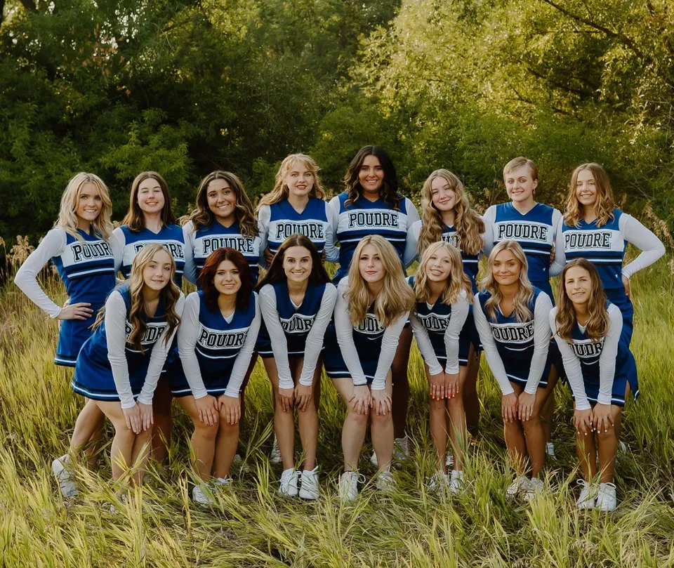 Un gruppo di giovani studentesse in uniforme da cheerleading posa insieme su un prato nel Poudre School District.