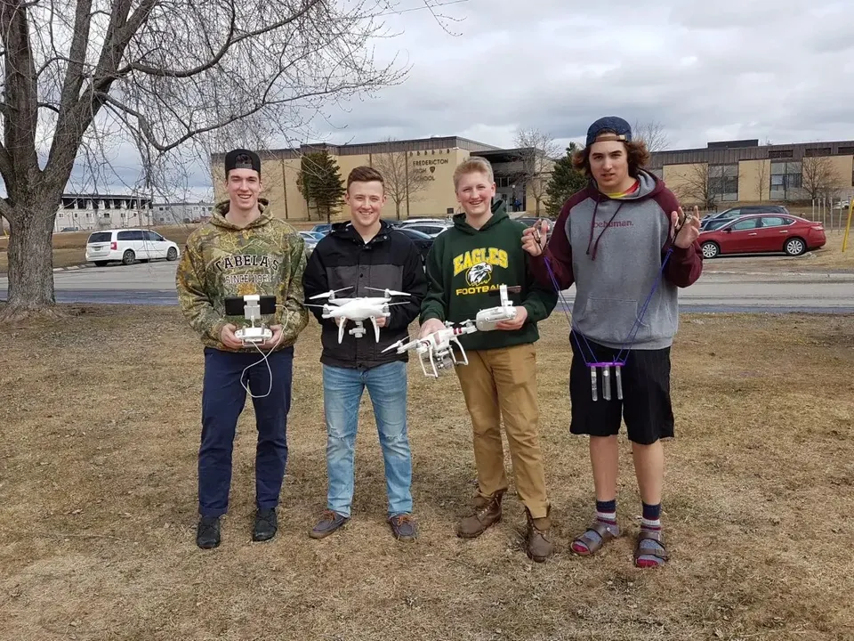 Un gruppo di studenti e studentesse si trova su un prato davanti agli edifici del campus della Fredericton High School.