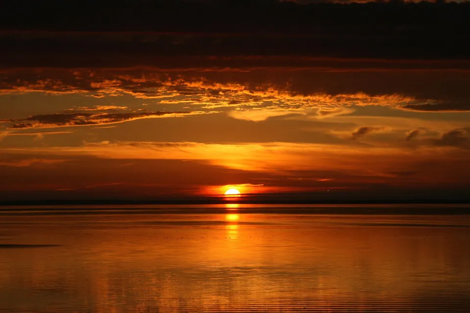 Un tramonto con il cielo arancione si riflette tranquillamente sull'acqua vicino alla Colonel Gray High School.