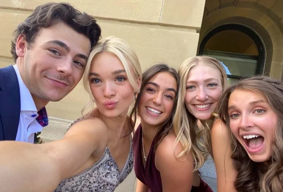 Un gruppo di studenti della St. Francis Xavier High School si scatta un selfie davanti a un cancello decorato con espressioni facciali divertenti.