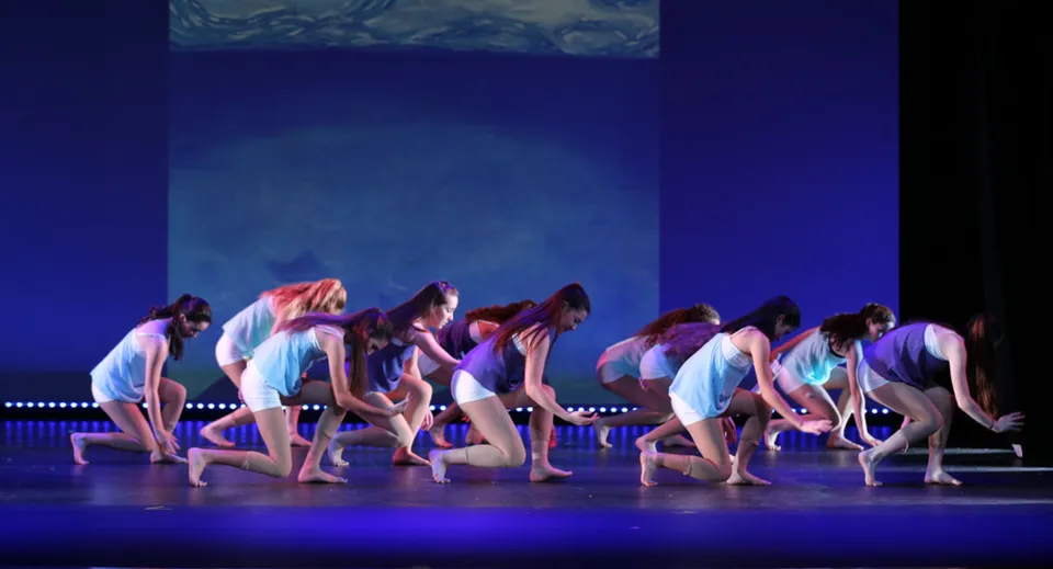 Un gruppo di studenti della Blackwater Community School si esibisce in una performance di danza sincronizzata su un palco con sfondo blu.