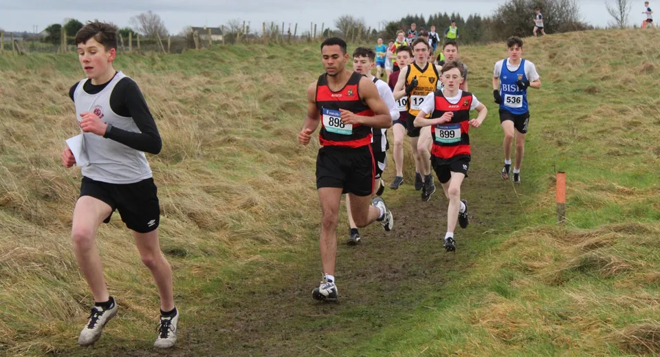 Atleti e atlete competono su un sentiero boschivo erboso durante la gara di corsa del St. Marys College Galway.