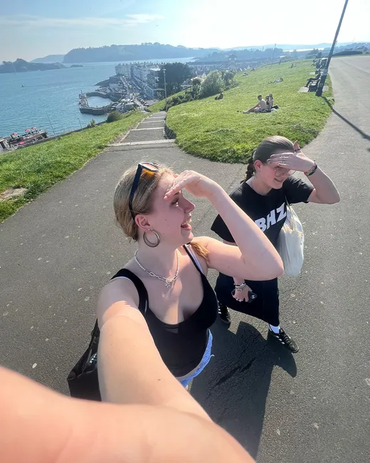 Dos estudiantes se hacen un selfie en un sendero con una bahía al fondo