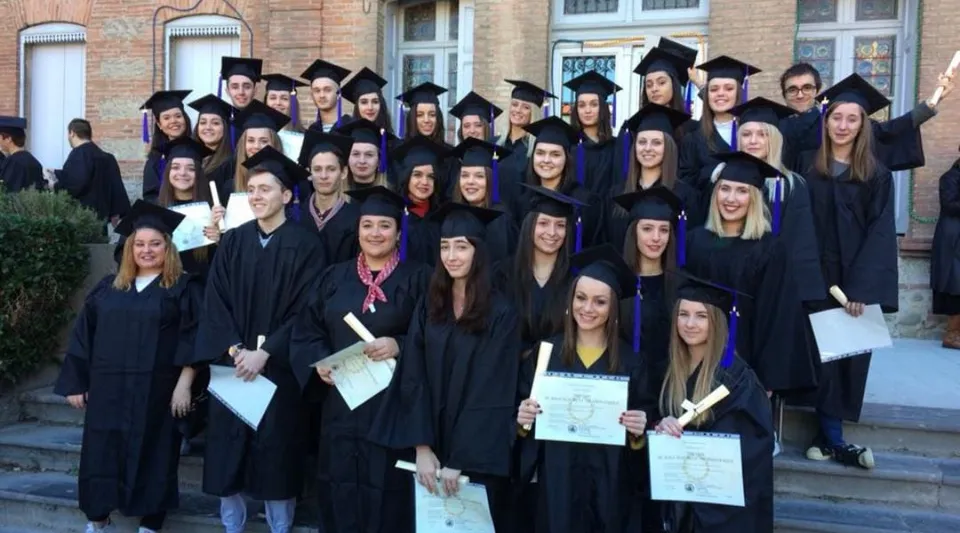 Un gruppo di diplomati del Lycée Notre Dame de Bon Secours è in piedi davanti a un edificio in mattoni con i propri diplomi in mano.