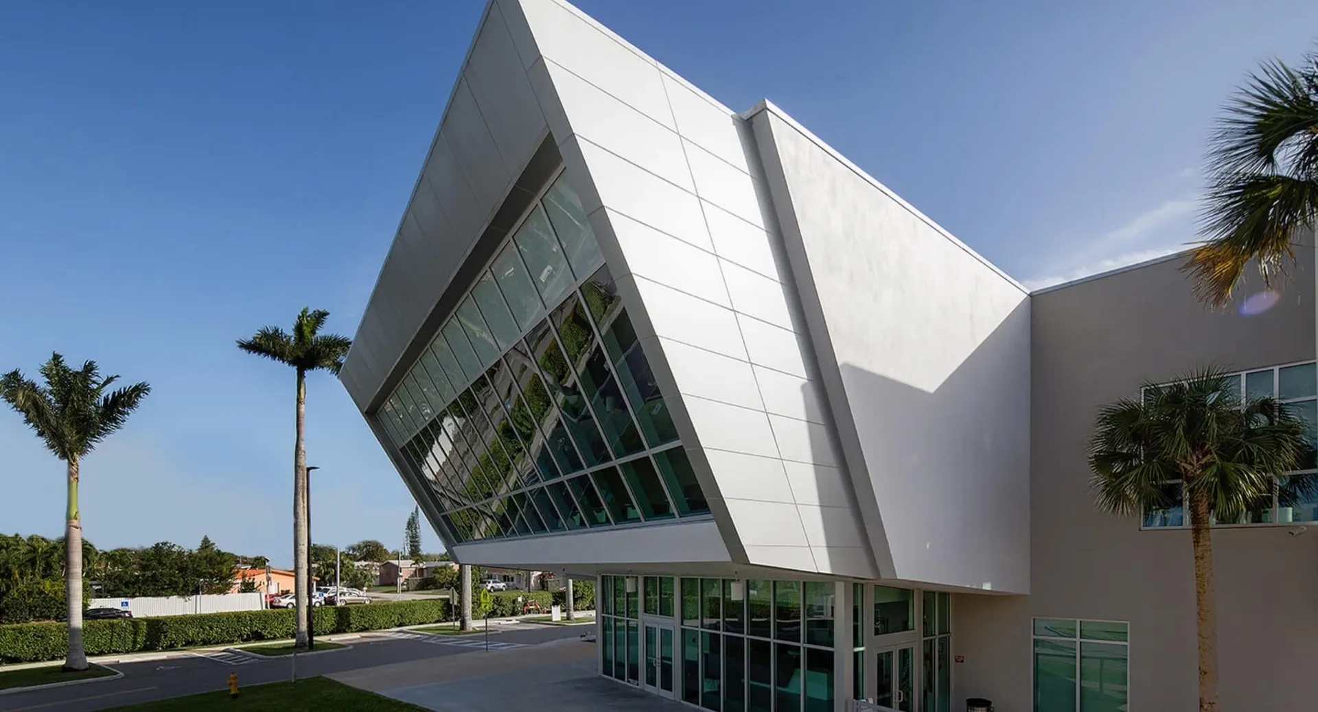 L'edificio moderno della St. Brendan’s Community School con ampie vetrate e palme in primo piano sotto un cielo blu.