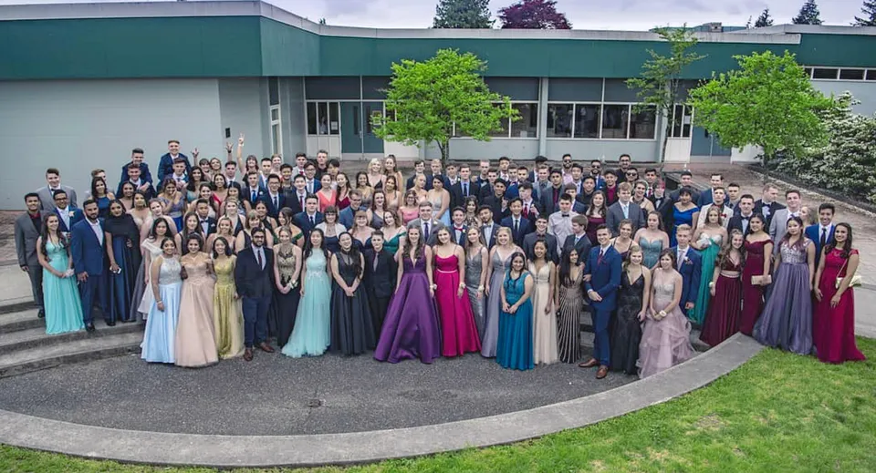 Un grande gruppo di studenti in abito formale si trova davanti all'edificio verde della Sands Secondary School.