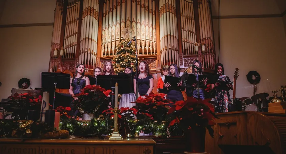 Un coro della Fulford Academy canta su un palco davanti a un grande organo in una chiesa decorata a festa.