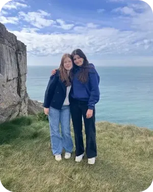 Due ragazze si abbracciano su una scogliera erbosa affacciata sul mare in Inghilterra