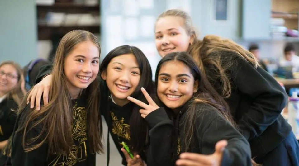 Un gruppo di studentesse sorridenti posa insieme nel campus della St. Timothy High School.