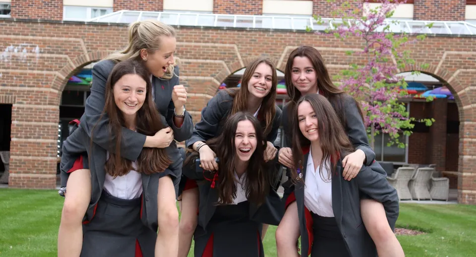 Un gruppo di diplomate della Battle Abbey School in toga si trova davanti a un edificio in mattoni con un albero in fiore.