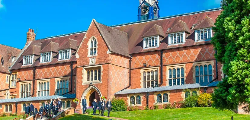 L'edificio storico in mattoni della Cranleigh School sorge in un'area verde con studenti e studentesse in primo piano.