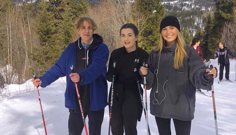 Tre studentesse della Mount Boucherie Secondary School sono in un bosco innevato e tengono in mano i bastoncini da sci.