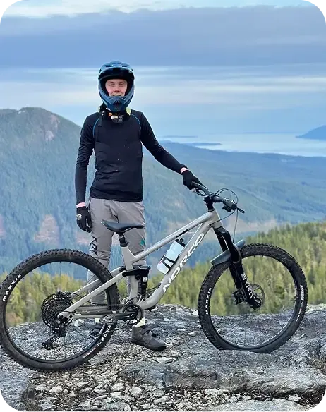Ragazzo in tenuta da mountain bike su una cima rocciosa con vista sui fiordi norvegesi