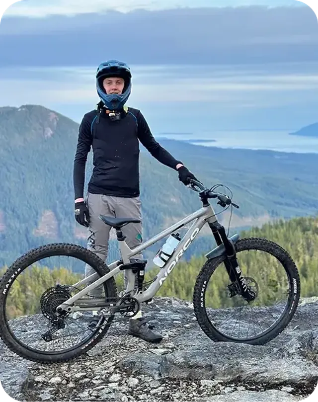 Ragazzo in tenuta da mountain bike su una cima rocciosa con vista sui fiordi norvegesi