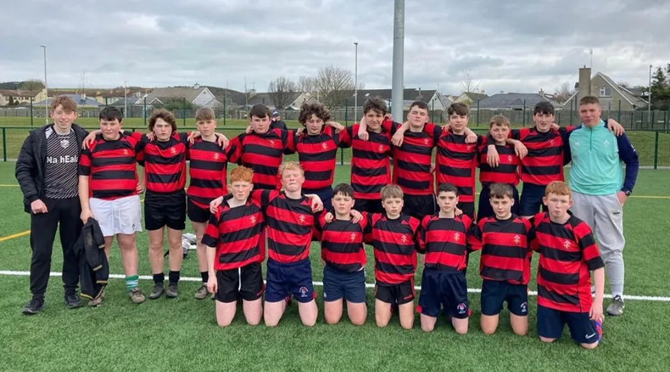 Un gruppo di studenti della Edmund Rice Secondary School si trova su un campo sportivo con maglie a strisce rosse e nere.