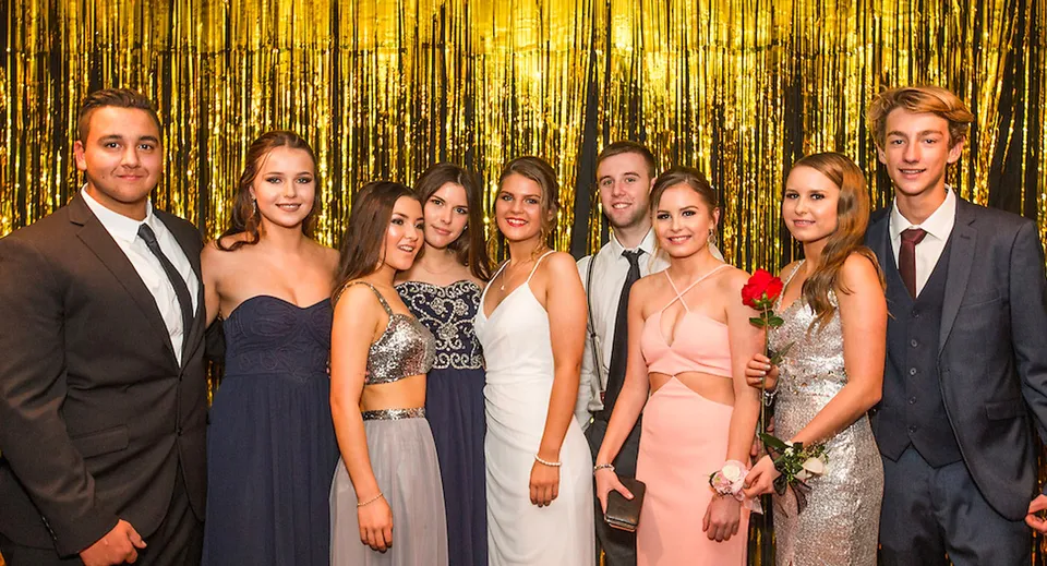 Un gruppo di studenti e studentesse ben vestiti si trova davanti a uno sfondo dorato e brillante nel campus della Mercury Bay Area School.