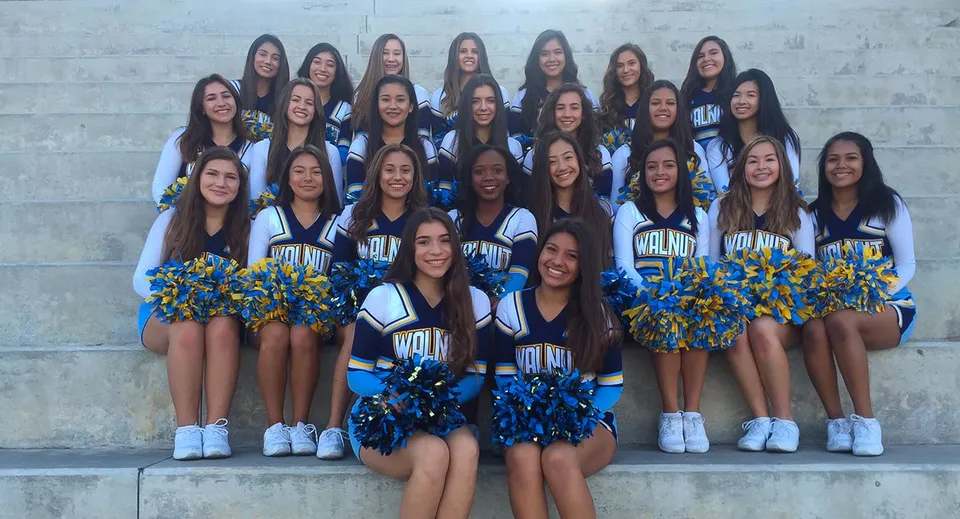 Un gruppo di cheerleader in divise blu e gialle posa davanti a un muro di cemento nel campus del Walnut Valley School District.