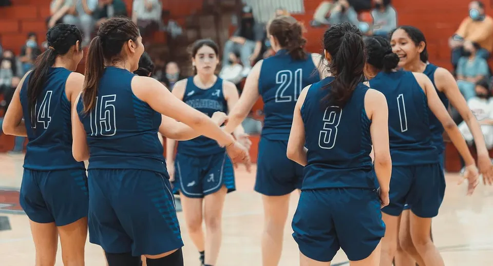 Un gruppo di giovani giocatrici di basket in maglia blu scuro si trova sul campo da basket dell'Anaheim Union High School District.