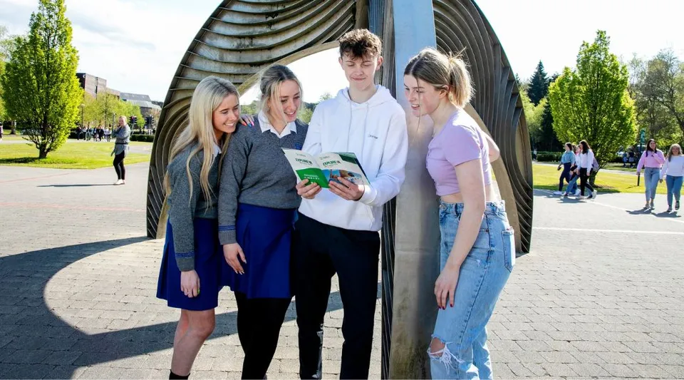 Un gruppo di studenti si trova all'aperto davanti a una caratteristica struttura architettonica nel campus della University of Limerick.