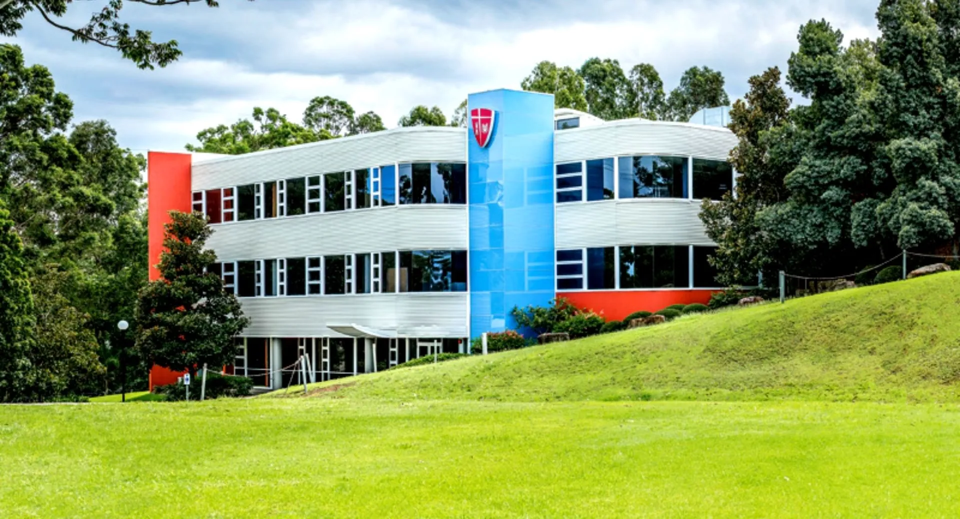 L'edificio moderno e colorato del John Paul College si trova su un pendio erboso ed è circondato da alberi.