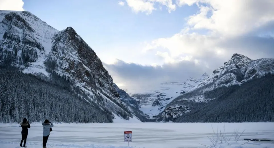 Due persone passeggiano vicino a un lago ghiacciato con montagne innevate sullo sfondo nei pressi della Sir Guy Carleton Secondary School.