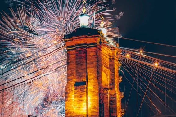 Fuegos artificiales iluminan el cielo nocturno detrás de la torre iluminada de un puente de piedra