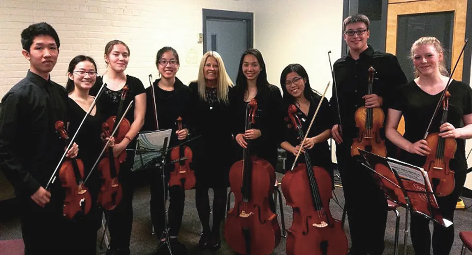 Un gruppo di musicisti con violini e violoncelli è insieme in un'aula del John Polanyi Collegiate Institute.