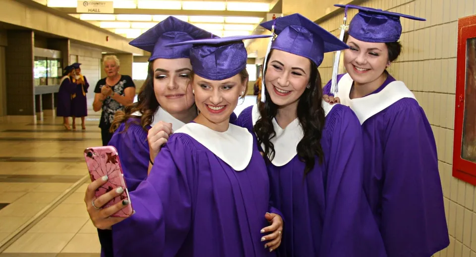 Studentesse della Sandwich Secondary School posano in toghe da diploma viola per un selfie nel corridoio.