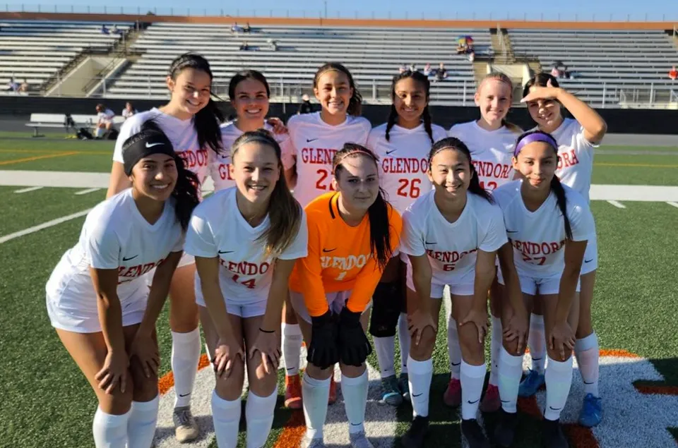 Un gruppo di giovani calciatrici in posa insieme sul campo sportivo della Chaffey High School con lo stadio sullo sfondo.