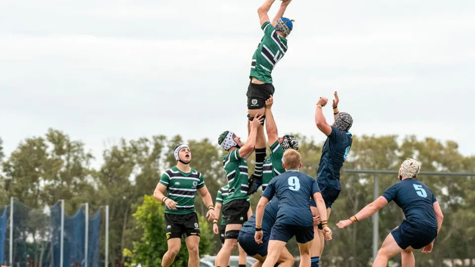 Un gruppo di studenti del Brisbane Boys' College che gioca a rugby durante una partita, con un giocatore che salta per afferrare la palla.