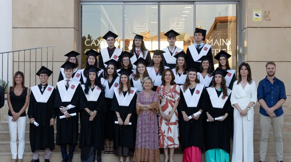 Un gruppo di diplomati in abito accademico posa davanti all'edificio con la scritta Campus Main del Caxton College.