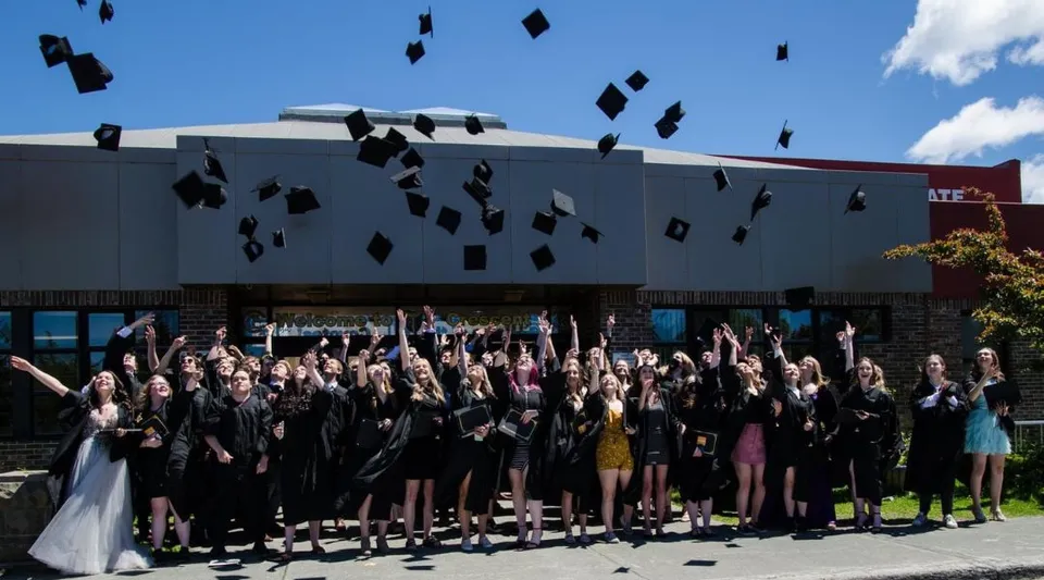 Un grande gruppo di diplomati del Crescent Collegiate lancia in aria i propri tocchi davanti a un edificio.