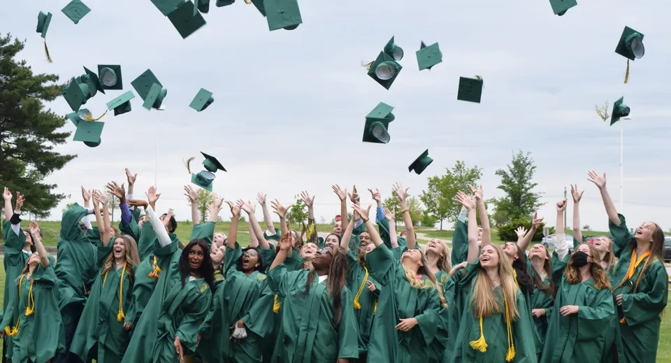 I diplomati della Alexandra Hills State High School lanciano i loro tocchi in aria davanti ad alberi e a un cielo nuvoloso.