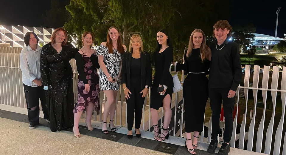 Un gruppo di studenti ben vestiti si trova di sera nel campus del Gawler and District College con alberi sullo sfondo.