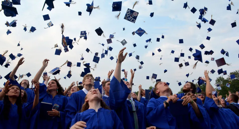 I diplomati della Marquette High School in toga blu lanciano i loro tocchi in aria.