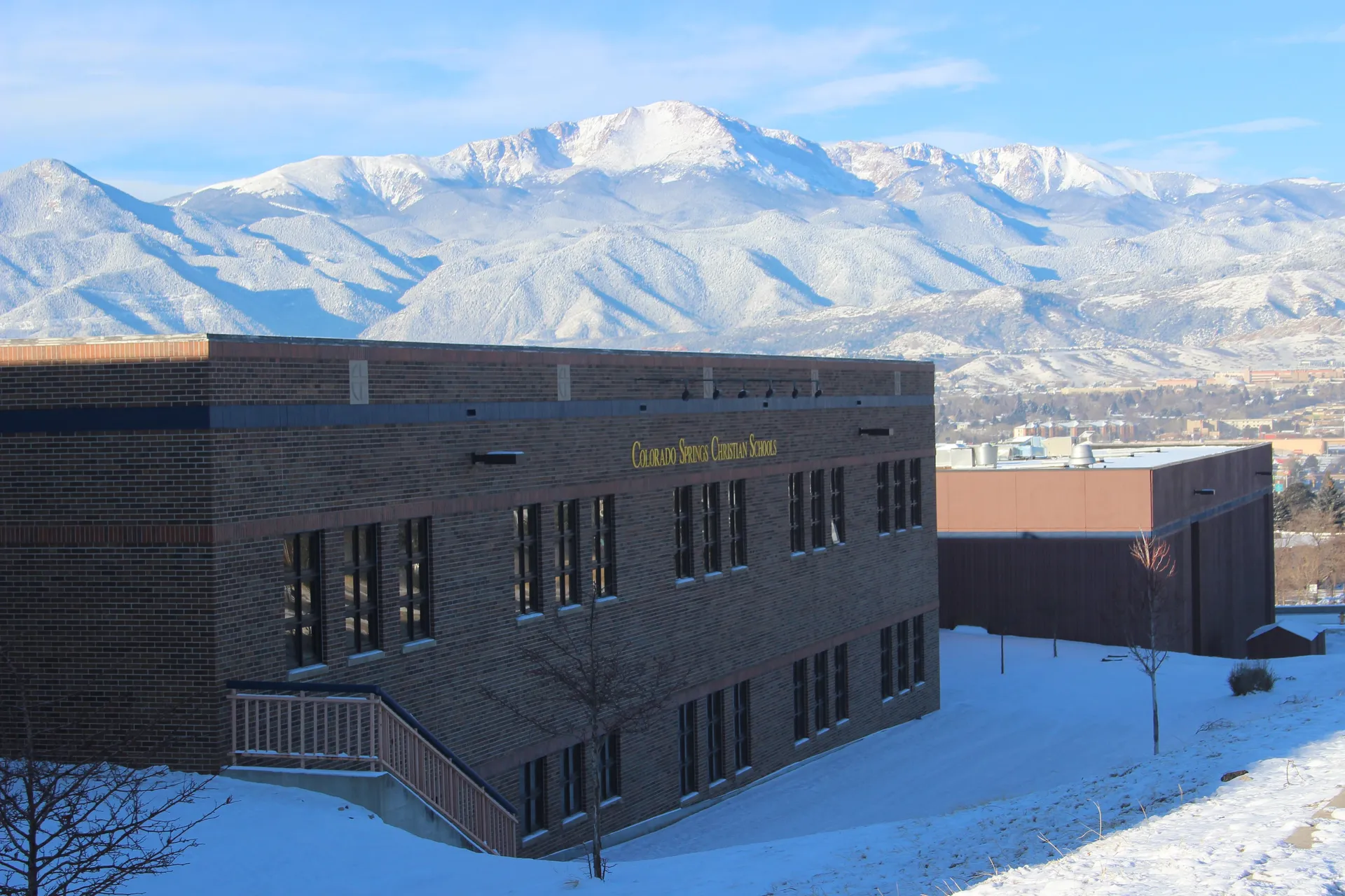 Un moderno edificio a più piani della Colorado Springs Christian School con montagne innevate sullo sfondo.