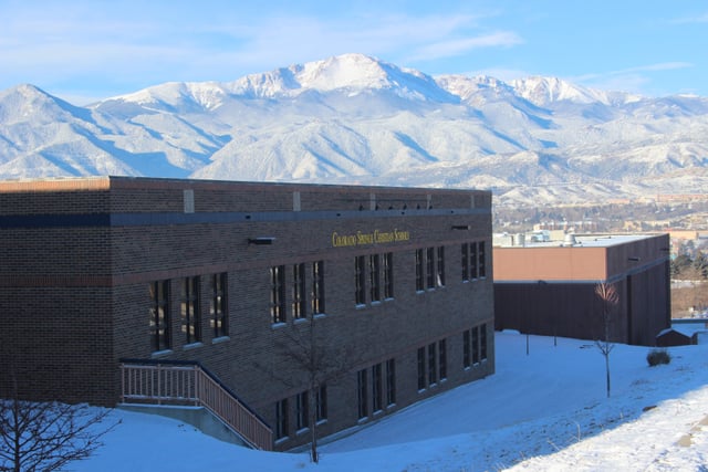 Ein modernes mehrstöckiges Gebäude der Colorado Springs Christian School mit schneebedeckten Bergen im Hintergrund.