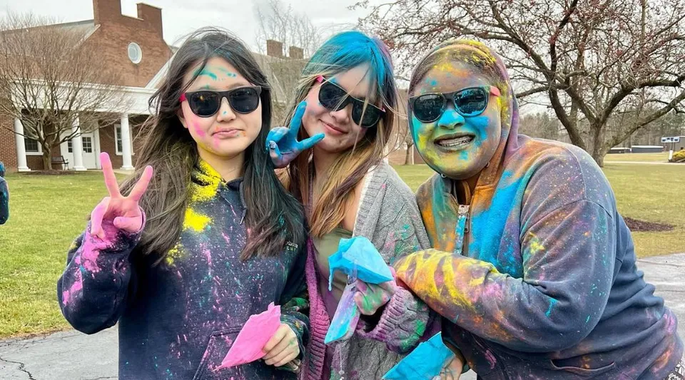 Tre studenti della Andrews Osborne Academy indossano abiti colorati e occhiali da sole davanti a un edificio residenziale immerso nel verde.