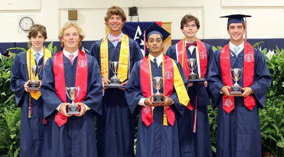I diplomati e le diplomate della Arendell Parrott Academy in abito accademico tengono trofei alla cerimonia di diploma su uno sfondo verde.